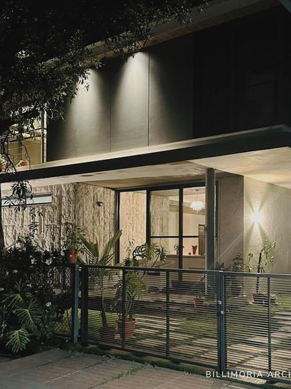 "Casa Magnifera" at night, with strategic uplighting that highlights the texture of the raw concrete walls and the form of the cantilevered structure.