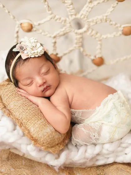 A close-up of a newborn girl in a boho-themed setup, sleeping peacefully with a dreamcatcher in the background.