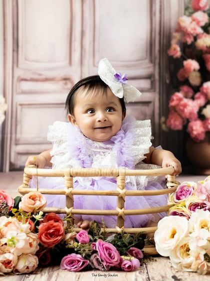 Twin girls in a beautiful floral setup, one dressed in purple, ready for their coordinated photoshoot.