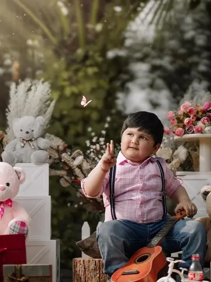 A three-year-old boy surrounded by teddy bears and flowers, looking up in wonder at a butterfly. This outdoor setup is full of color and joy.