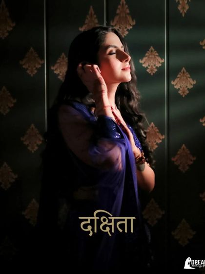 A beautiful solo portrait of the bride, with her name "Dakshita" in Hindi, captured in a moment of quiet reflection with dramatic lighting.
