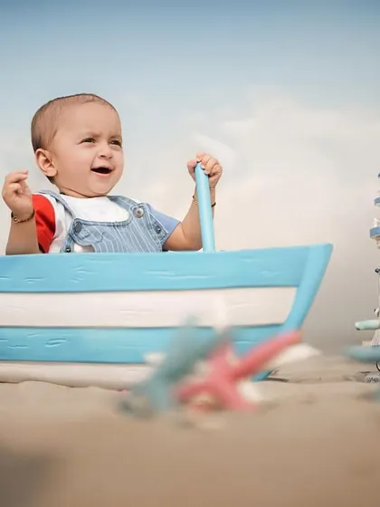 A little sailor ready for an ocean adventure. This beach setup with a toy boat and nautical props is perfect for a fun and imaginative photoshoot.