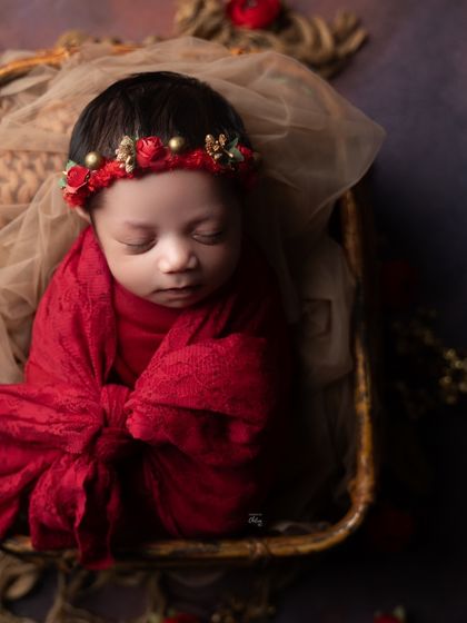 A peaceful portrait of a baby wrapped in luxurious red fabric, looking like a precious gift.