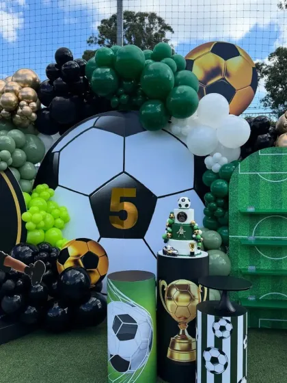 The complete dessert setup for the football party, showcasing the cake, trophy, and themed stands against the giant football backdrop.