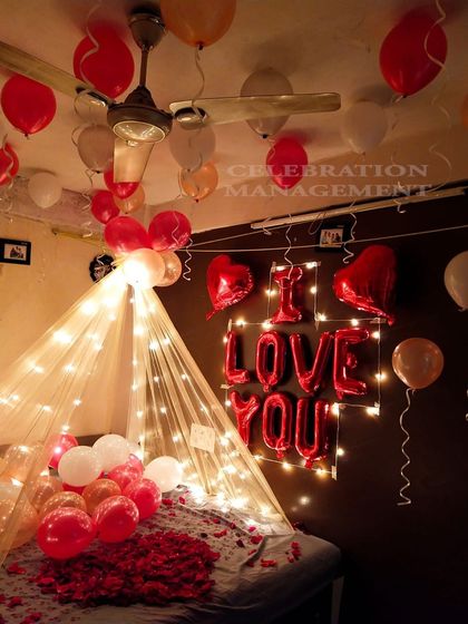 Here is another beautiful canopy setup, perfect for a birthday or anniversary. The bed is covered in rose petals, with 'I LOVE YOU' foil balloons and fairy lights on the wall behind it, creating a warm and loving ambiance.