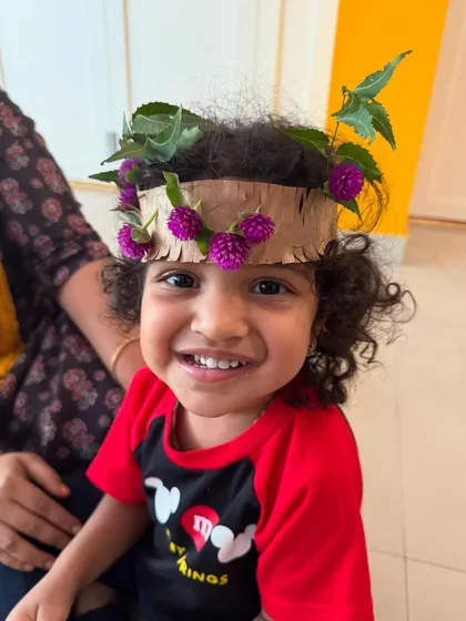 The proud smile of a child wearing her own handmade nature crown. Adorned with leaves and bright purple flowers, this simple craft allows kids to feel connected to the beauty of the outdoors.