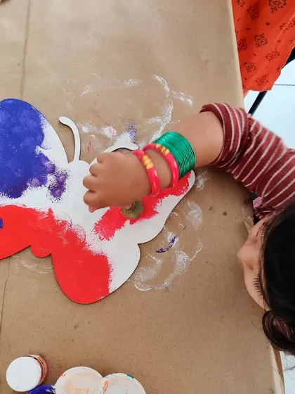 A toddler enjoying a sensory art experience, using a sponge to paint a butterfly in the colors of the flag.