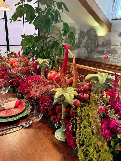 The full length of the harvest-style table runner, abundant with red florals, fruits, and greenery, creating a feast for the eyes.
