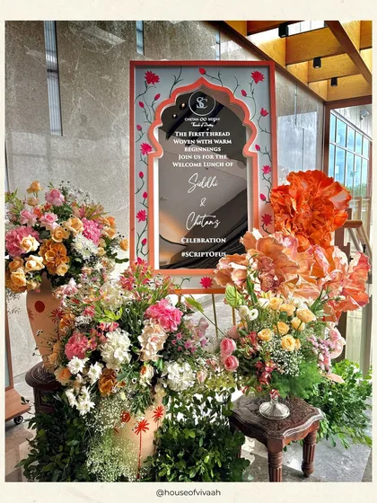 A personalized welcome sign for the couple, framed by an arch of vibrant peach and pink florals, creating a beautiful and memorable entrance moment.