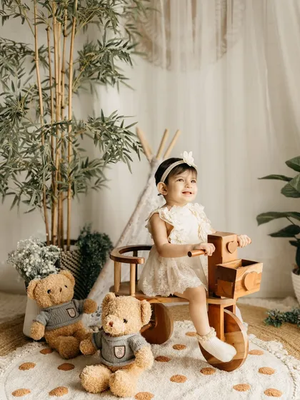 A candid moment of this little girl playing on a wooden tricycle in the neutral, plant-filled studio.