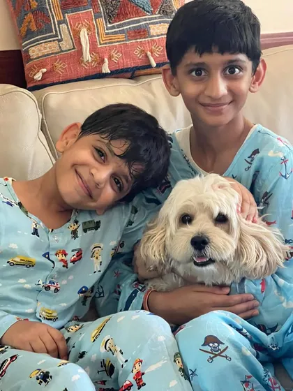 Two boys in matching pajamas cuddle with their happy Cavapoo.