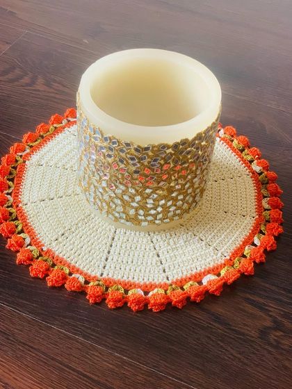A cream-colored doily with an orange tulip border, shown here under a candle holder.