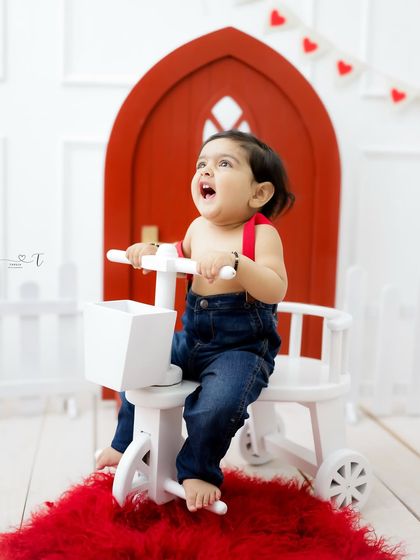 A cheerful little boy on his tricycle. The bright red door and heart garland add a touch of playful charm to this valentine-themed setup.