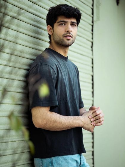 A medium shot showing more of the pose and outfit. The model's stance against the wall creates a casual yet confident vibe, perfect for showcasing everyday men's fashion and streetwear.