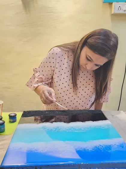 A student creating a black sand sea effect on a piece of wall decor during a workshop.