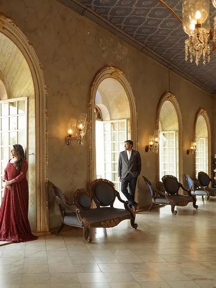 A couple stands framed in an ornate archway of a palace hall, with grand chandeliers and marble floors creating a sense of timeless elegance. This pre-wedding shoot in Hampi showcases how I use architectural elements to create stunning, regal portraits.