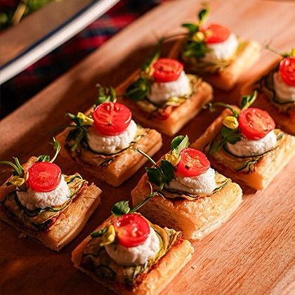 Zucchini and goat cheese tartlets topped with a fresh cherry tomato. The combination of flaky pastry, creamy cheese, and fresh vegetables makes this a popular vegetarian canapé.