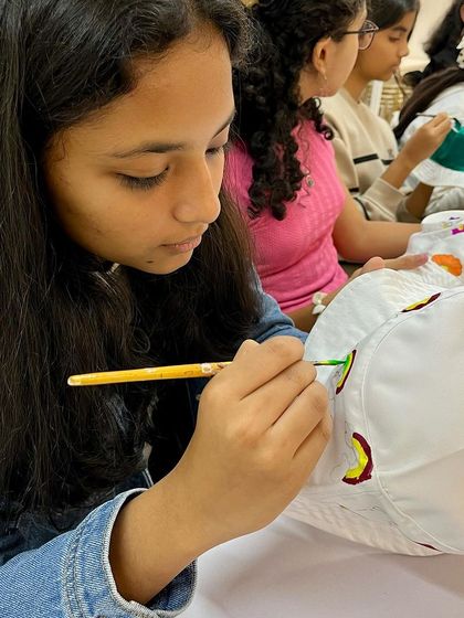 A teenager concentrates on adding details to her bucket hat during a fun and social art party.