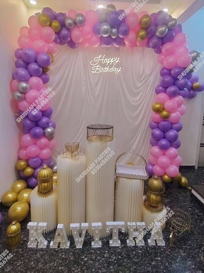 A beautiful birthday stage setup with a pink, purple, and gold balloon arch and elegant props.