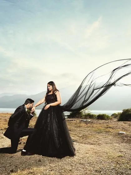 A dramatic pre-wedding shot at Tehri lake, with the groom kissing the bride's hand as her black gown flows in the wind. This image has a grand, cinematic feel.