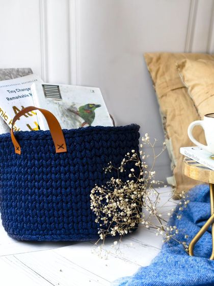 Another view of the navy blue crochet basket, styled in a serene corner with a cup of tea and a blanket. This image evokes a sense of calm and relaxation, perfect for home decor.