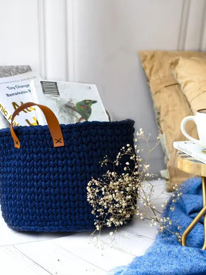 Another view of the navy blue crochet basket, styled in a serene corner with a cup of tea and a blanket. This image evokes a sense of calm and relaxation, perfect for home decor.