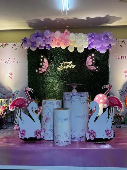 This is a duplicate of ID 6, 39, 181. A whimsical garden theme combining butterflies, flamingos, and swans. The backdrop is a lush green wall with a neon sign, surrounded by pastel balloon garlands and cute props.