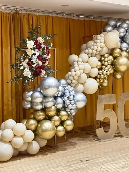 A glamorous setup for a 50th birthday celebration. The organic balloon garland in shades of white, gold, and silver is paired with large "50" marquee numbers and a floral arrangement for an elegant touch.