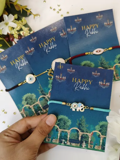 A hand holding a selection of our evil eye and elephant charm Rakhi bracelets, ready for gifting.