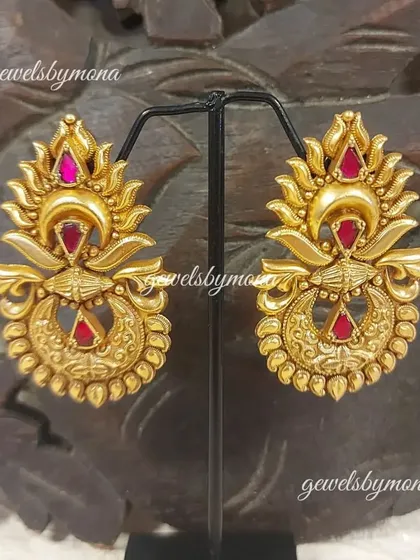 A variation of the ornate Dakshinaya earrings, this time with vibrant ruby-colored stones. The craftsmanship highlights the sun and moon motifs popular in temple jewellery design.