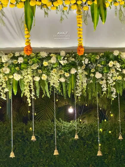 A close-up of the mandap's floral ceiling, showing the intricate arrangement of white flowers, greenery, and hanging temple bells.