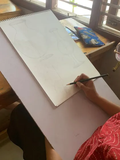 A student works on still life sketches of vases. This practice helps develop observational skills and an understanding of form and proportion.
