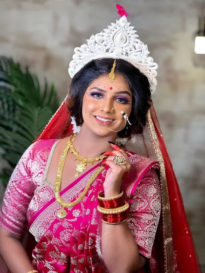 A close-up of the Bengali bride, highlighting the intricate white and red 'bindi' design on the forehead and the vibrant purple eyeshadow.