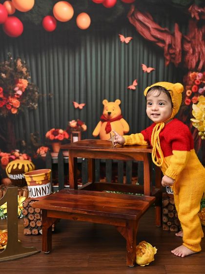 A trip to the Hundred Acre Wood with Winnie the Pooh. This charming setup, complete with "hunny" pots and autumn colors, is perfect for capturing the sweetness of your little one.