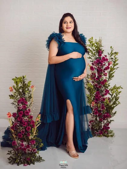 A full-length view of this stunning teal gown. The floral arrangements on either side frame her beautifully, adding color and life to the portrait.