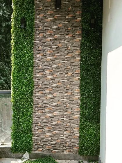 The completed balcony wall decor before the final cleanup, showing the combination of stone texture and lush green panels.