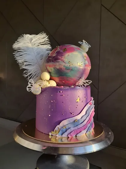 Isn't she gorgeous? I made this dreamy cake for a little girl who loves pink and purple. It features a galaxy-like chocolate sphere, delicate butterflies, and a white feather for a magical touch.