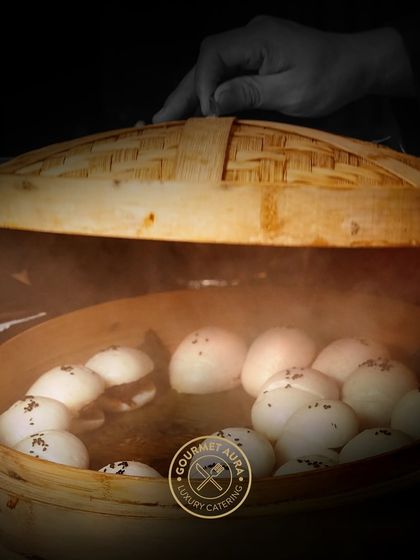 A hand lifts the lid of a bamboo steamer, revealing perfectly steamed buns. This simple act represents the care and anticipation we build into our dining experiences.