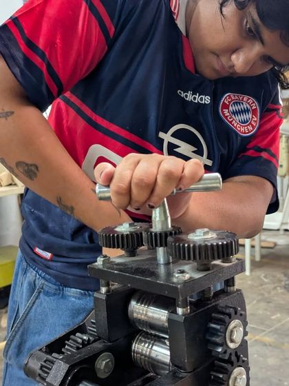 A participant uses the rolling mill, a specialized piece of equipment that flattens and shapes the sterling silver ingot into a workable sheet or wire for her jewelry project.