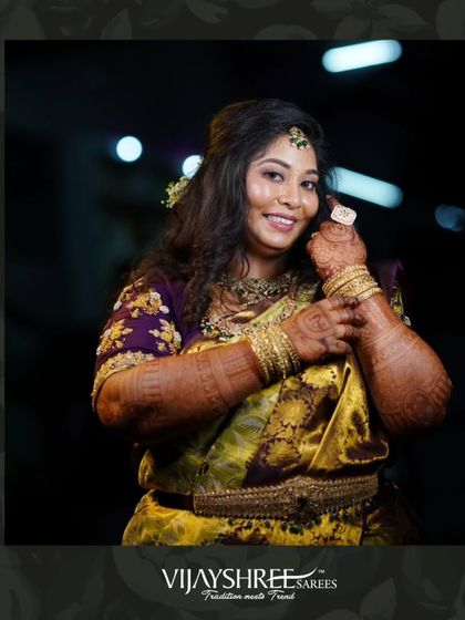 A happy client glowing during her wedding festivities, adorned in a rich yellow and purple brocade Kanjivaram.