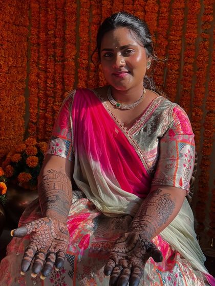 Tejashree seated amidst a beautiful marigold setup, her hands open to display the intricate henna work.