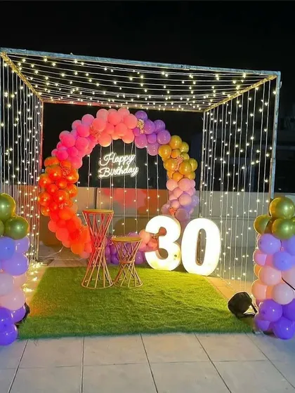 A colorful cabana setup for a 30th birthday, using a rainbow balloon arch and light-up numbers.