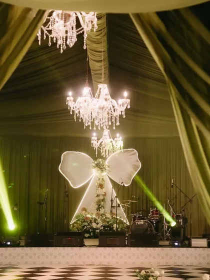 A dramatic view of the "Big Bow Affair" stage, framed by lush olive green drapes. The crystal chandeliers and checkered dance floor added to the glamorous, fairytale-like ambiance.