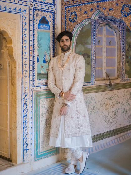 A regal groom portrait, with the groom standing against a beautifully painted wall in a classic Jaipur palace.