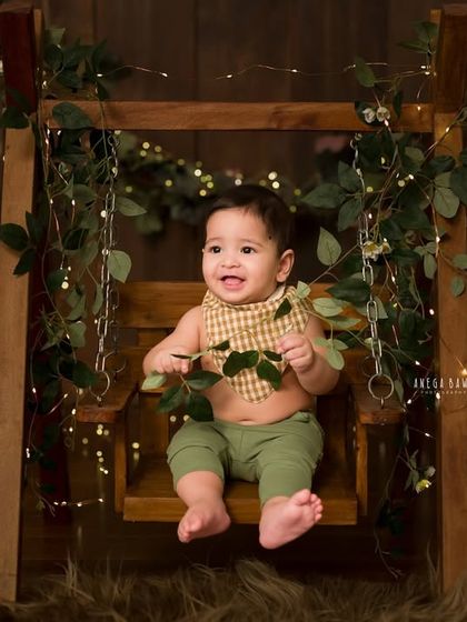 A moment of pure delight on a miniature swing. The combination of the rustic props, greenery, and twinkling lights creates a magical setting for this milestone portrait.