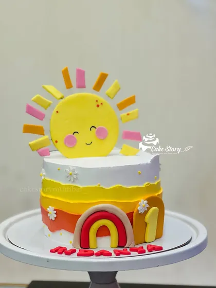 A 'You Are My Sunshine' themed cake for a first birthday. The cheerful sun topper and warm-colored rainbow create a bright and happy design for a little one's special day.
