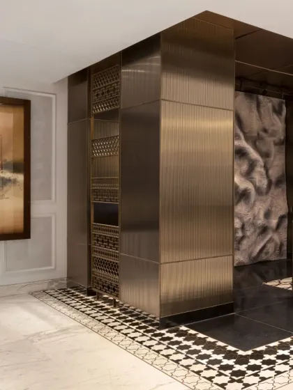 The design uses a deliberate color transition, moving from light marble to dark flooring, to draw visitors toward the reception desk. This visual shift is reinforced by architectural elements like the intricately detailed columns and the sculptural backdrop.