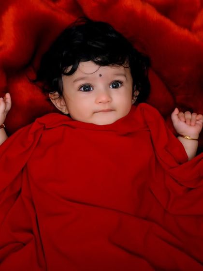 A striking portrait of a baby wrapped in vibrant red fabric against a matching red background. The bold color makes this a powerful and memorable image.