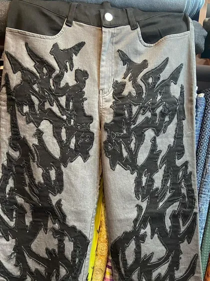 A closer look at the texture and application of the abstract appliqué on the grey denim jeans. This shows how different fabrics can be layered for a dramatic effect.