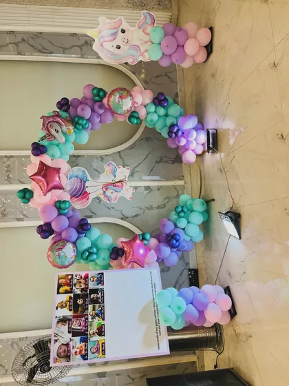 A magical unicorn-themed ring decoration for a birthday party. The balloon arch uses pastel shades of purple, pink, and teal, with unicorn cutouts and star-shaped foil balloons.